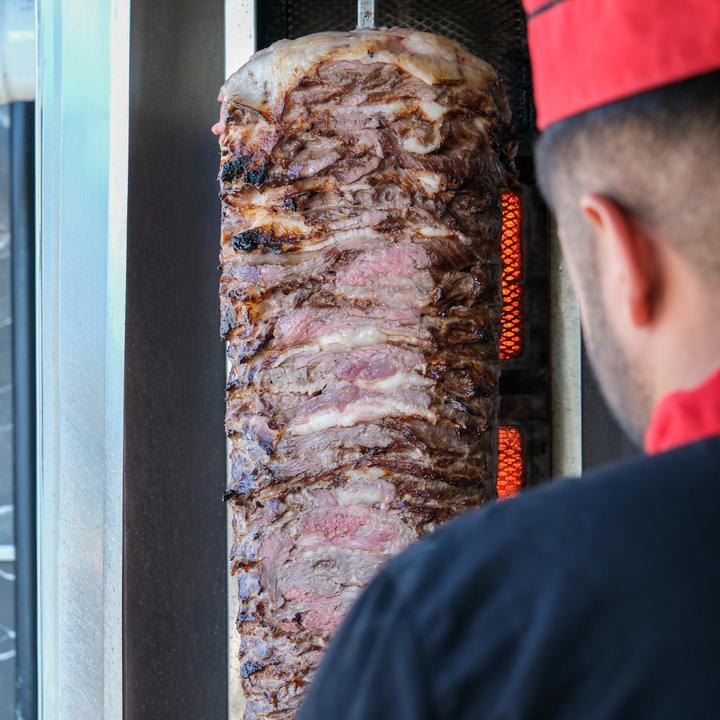 Ocakta pişen et döner ve başında kırmızı şapkalı usta
